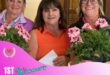 Three white women standing next to each other holding big bunches of flowers, the one in the middle wearing an orange shirt.