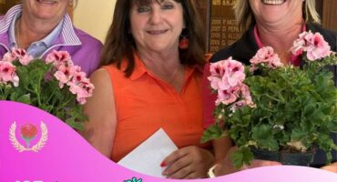 Three white women standing next to each other holding big bunches of flowers, the one in the middle wearing an orange shirt.