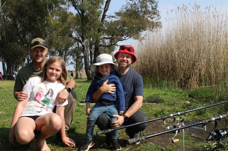 Two men and children posing next to fishing rods