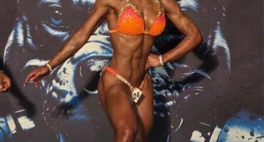 A female bodybuilder wearing an orange bikini on stage during a competition.