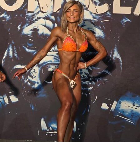 A female bodybuilder wearing an orange bikini on stage during a competition.