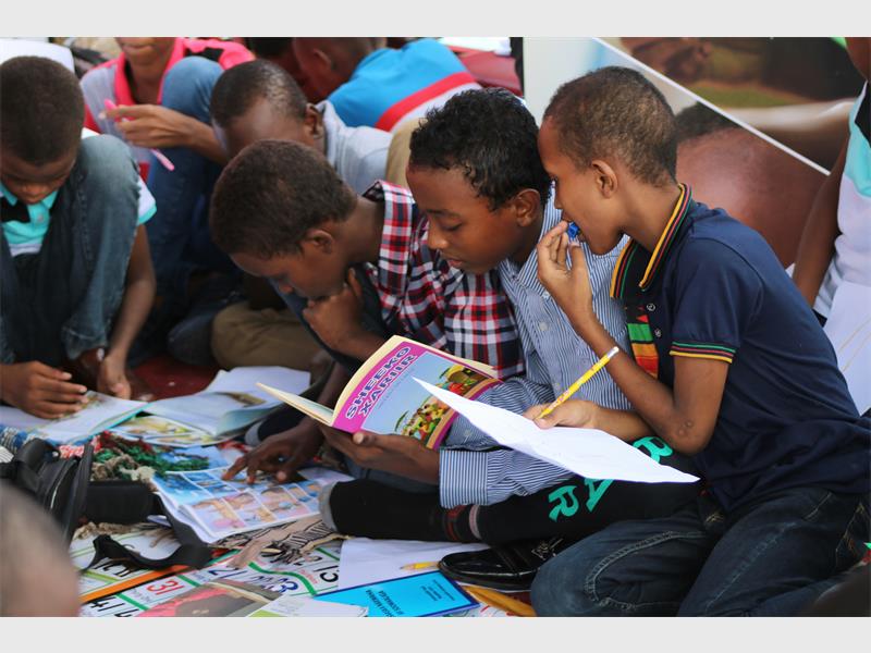 A group of black children sitting on the floor pouring over open books.