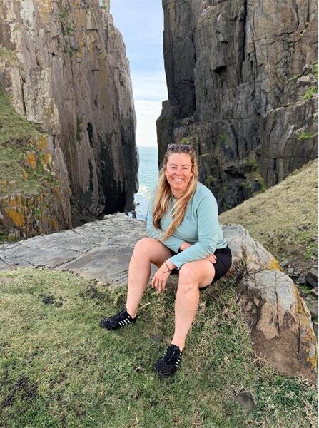 A lady sitting on rocks, wearing black shorts and a green jacket