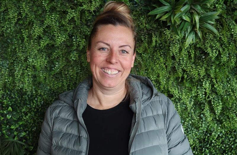 A lady smiling wearing a black top and green jacket