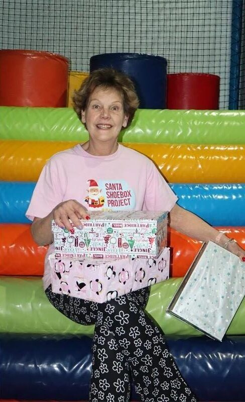 Lady in a pink top and black pants, holding wrapped boxes