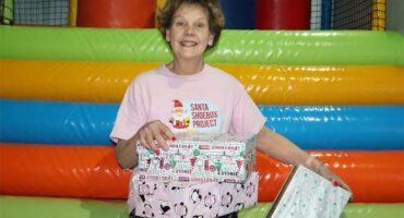 Lady in a pink top and black pants, holding wrapped boxes
