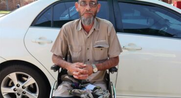 White man with grey bread sitting on a wheelchair.
