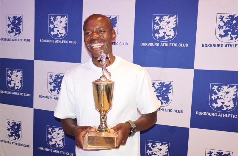 A man wearing a grey sweater, holding a trophy.