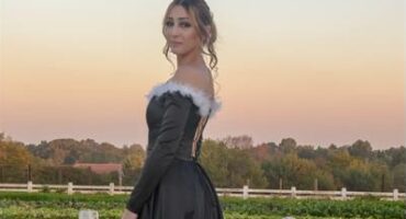 Girl in a black dress with white detailing standing in front white fence at sunset