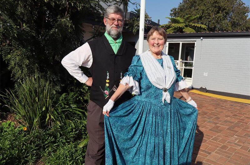 A man in a brown suit next to a lady wearing a green dress.