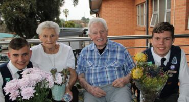 Twee jong seuns hou blomme aan bejaarde man en vrou