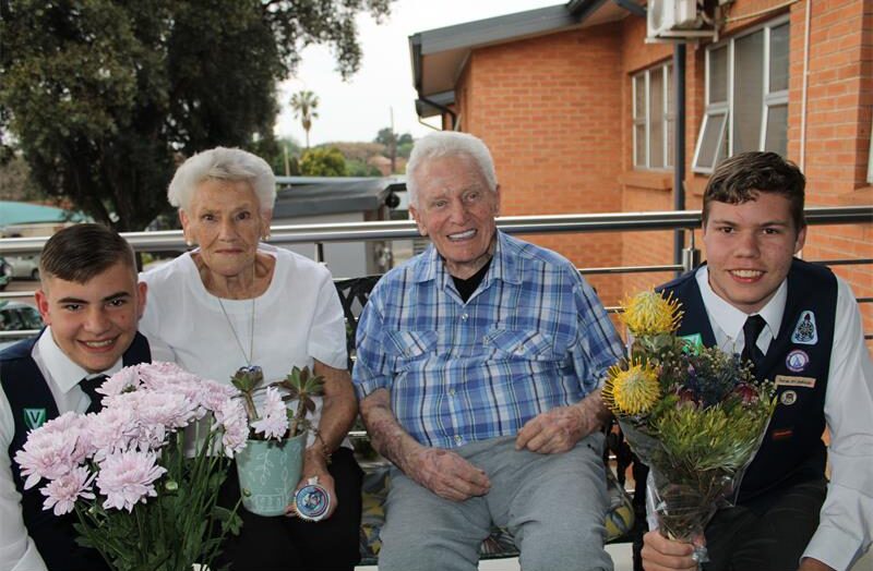Twee jong seuns hou blomme aan bejaarde man en vrou