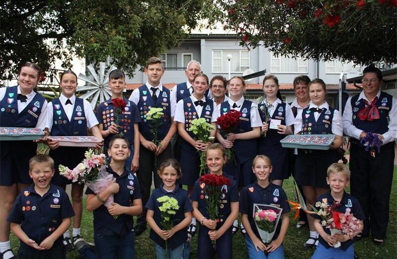 Groep kniders in univorms wat blomme en kolwyntjies vas hou