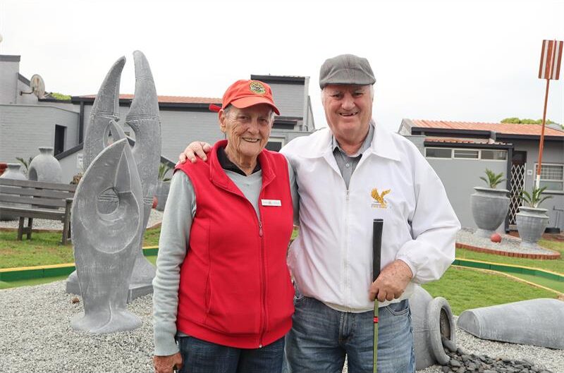 A old lady in a red jacket standing next to a man wearing a white jacket
