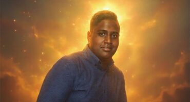 An indian boy smiling wearing a jean shirt.
