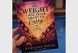 A book cover with the words the weight I was never meant to carry and hand holding the book.