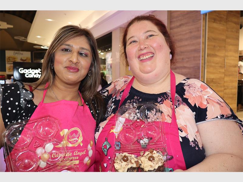 two women dressed in pink apron and both holding cupcakes