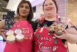 two women dressed in pink apron and both holding cupcakes