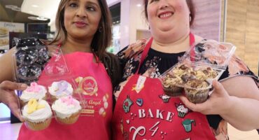 two women dressed in pink apron and both holding cupcakes