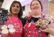 two women dressed in pink apron and both holding cupcakes