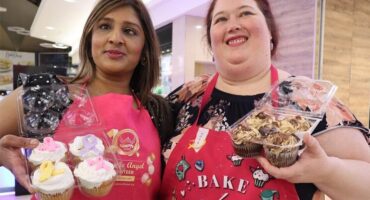two women dressed in pink apron and both holding cupcakes