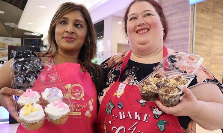 two women dressed in pink apron and both holding cupcakes