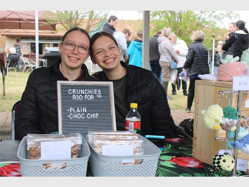 Two young white girls behind a table displaying crafts.