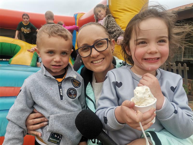 A white woman with two white children, a boy and girl, with a jumping castle in the background.