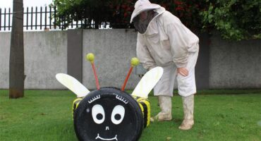 Man wearing a bee suit standing next to a bee made out of tyres