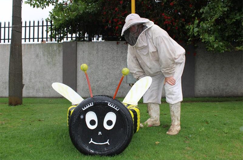 Man wearing a bee suit standing next to a bee made out of tyres