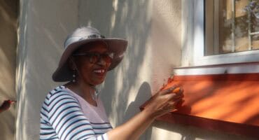 Coloured woman wearing a hat, repainting a window sill