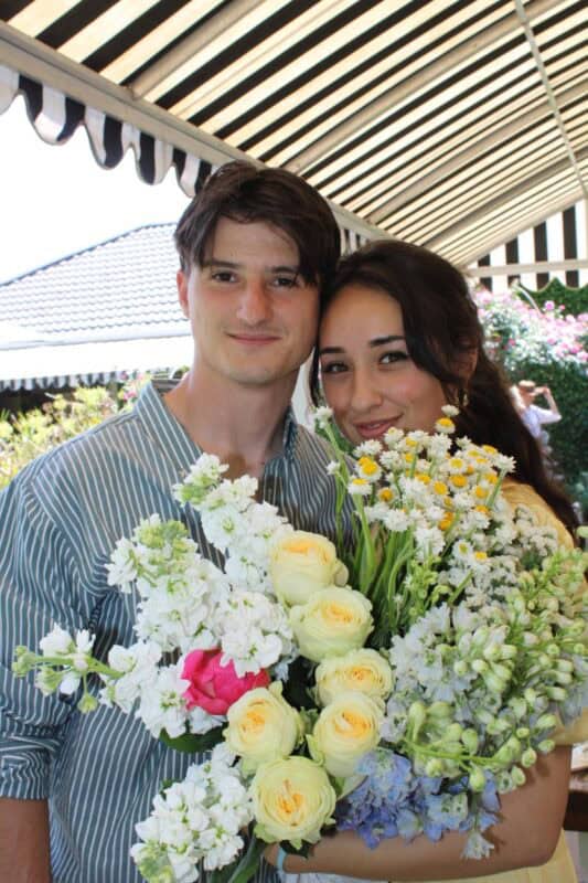 Young white couple smile from behind a bouquet of flowers