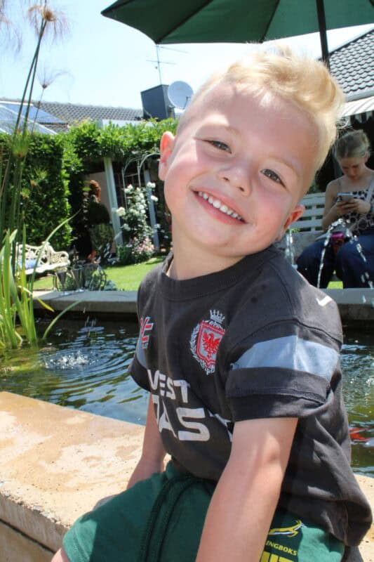 Young boy sitting next to a fish pond
