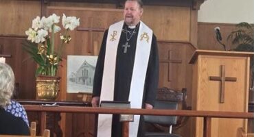 White reverend standing in front of a church congregation
