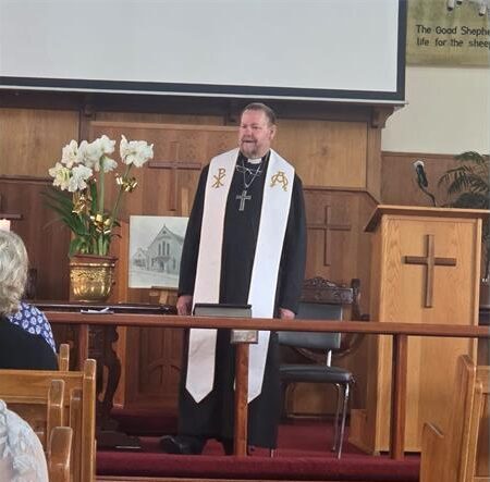 White reverend standing in front of a church congregation