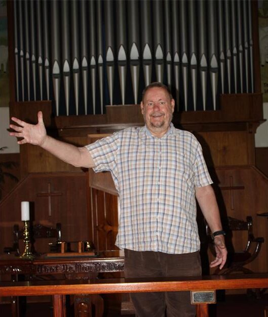 White man standing in front of a church with his right hand extended into the air