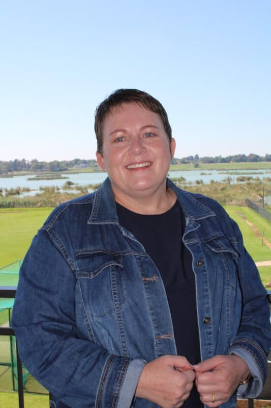 Short-haired woman wearing denim jacket standing on a balcony over looking a dam