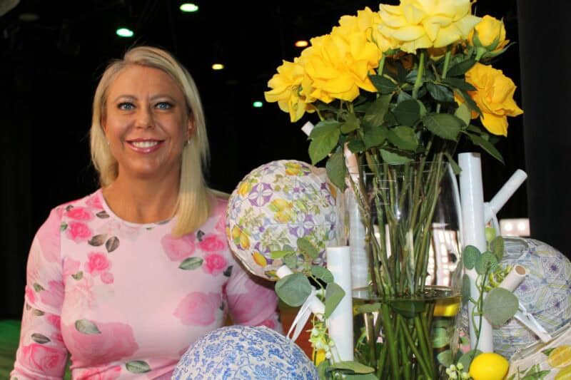 Blonde woman wearing pink standing next to yellow roses