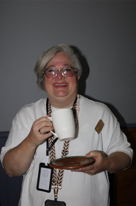 Woman with grey hair holding a mug and wooden saucer