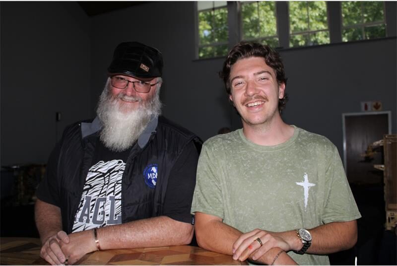 Two men leaning on a wooden table