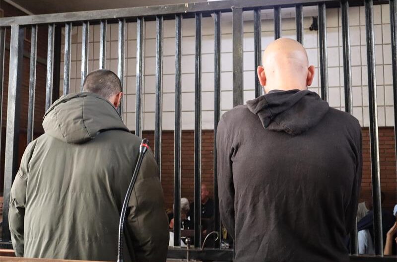 Two men photographed from the back, one in a green jacket and one in a black hoodie