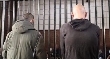 Two man standing next to each other one in a green jacket and one in black hoodie.