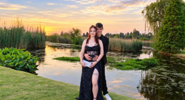 Young man and girl in evening wear pose in front of a dam at sunset