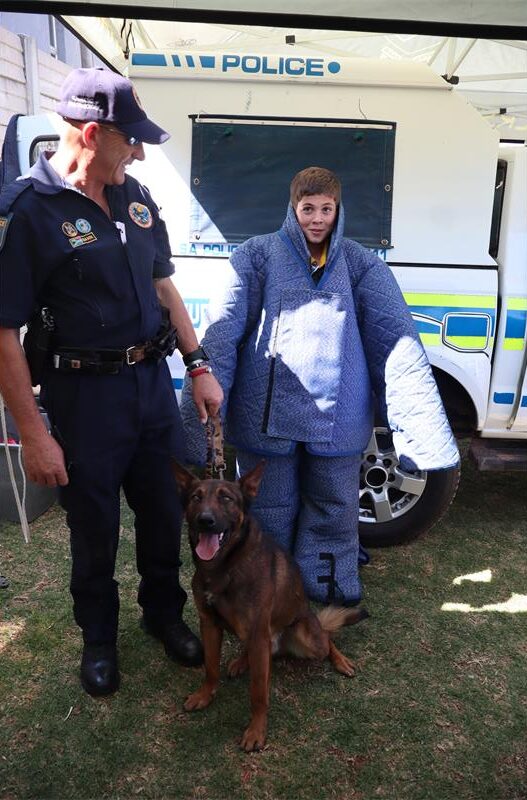 A policeman standing with his k9 dog and a boy wearing protective wear.