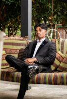 Indian boy wearing a black suit and white shirt sitting on a stripped couch.