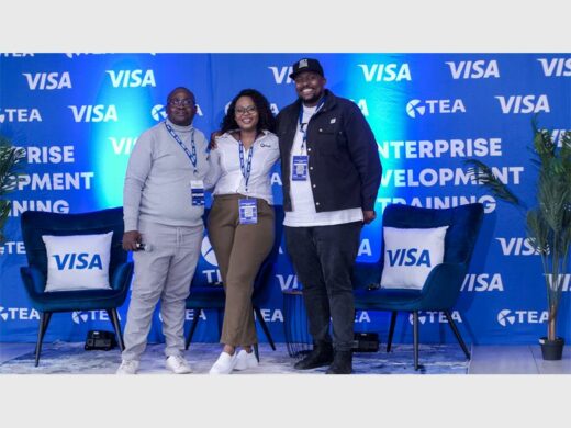 Two black males flanking a black female, all wearing lanyards with a VISA banner in the background.