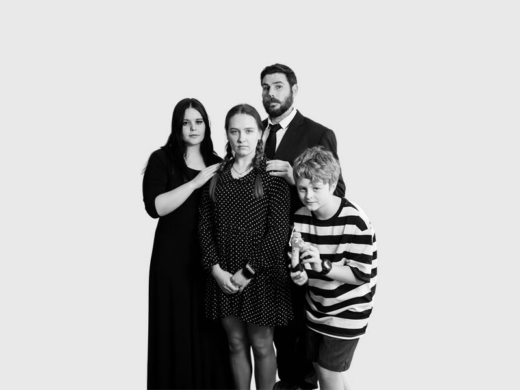 Black and white photo of four people dressed for a production of the Addams Family. 