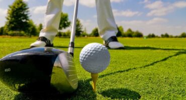 Sourced image of a golf ball on an tee with a club, with a golfer about to tee off.