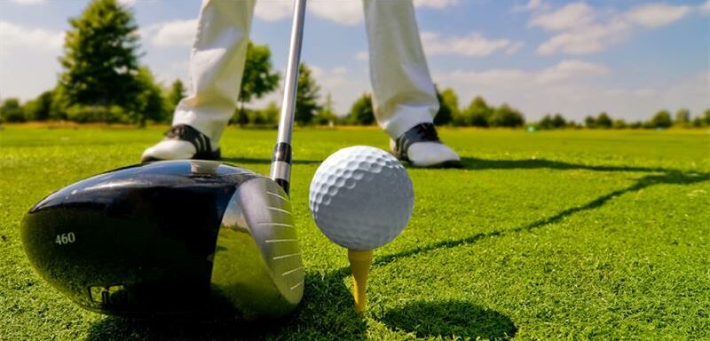 Sourced image of a golf ball on an tee with a club, with a golfer about to tee off.