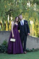 Girl wearing a deep purple dress, holding a sliver handbag, with a boy wearing a black suit and purple tie